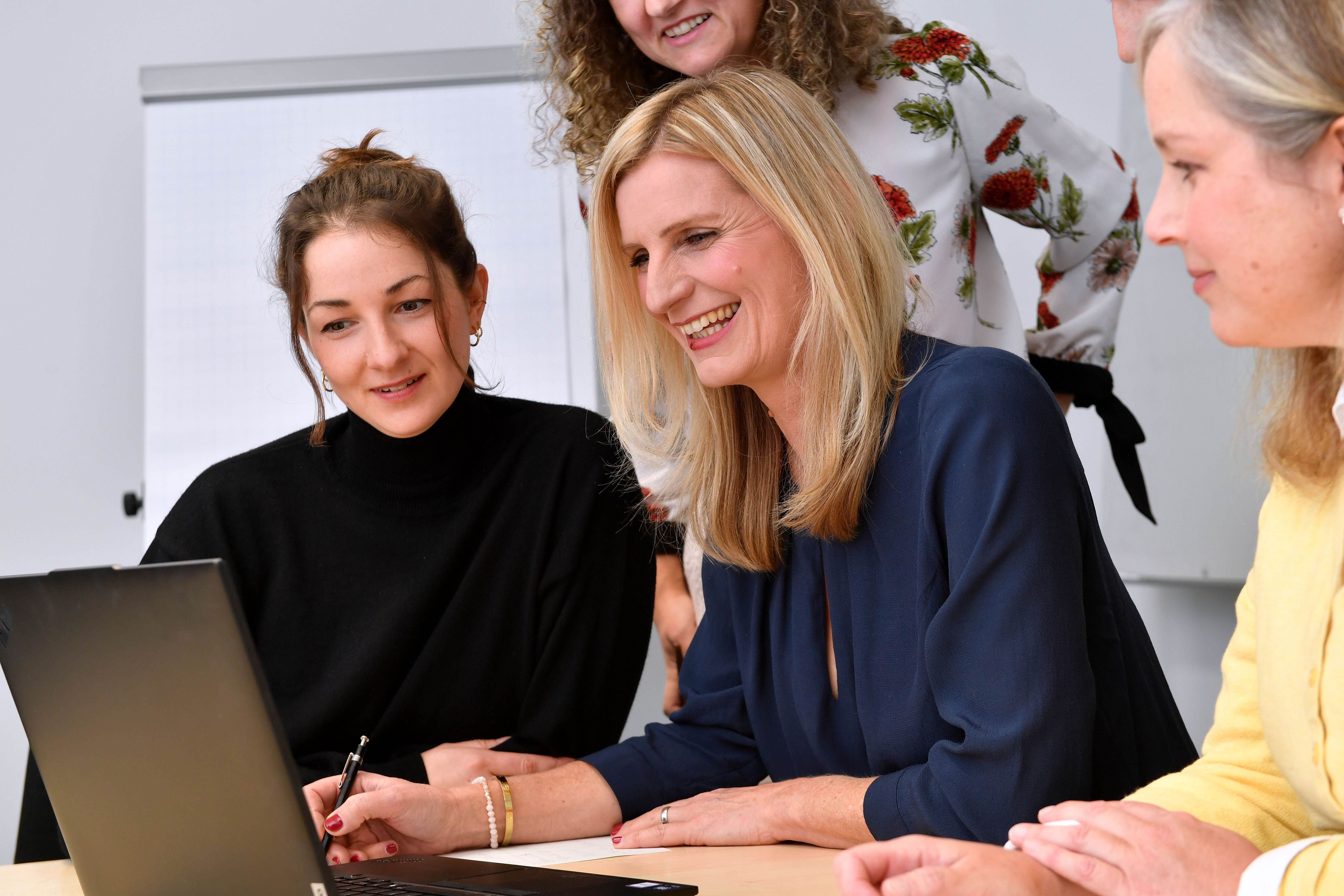 Mehrere Menschen sitzen in einer Besprechung. Vor ihnen steht ein Laptop.