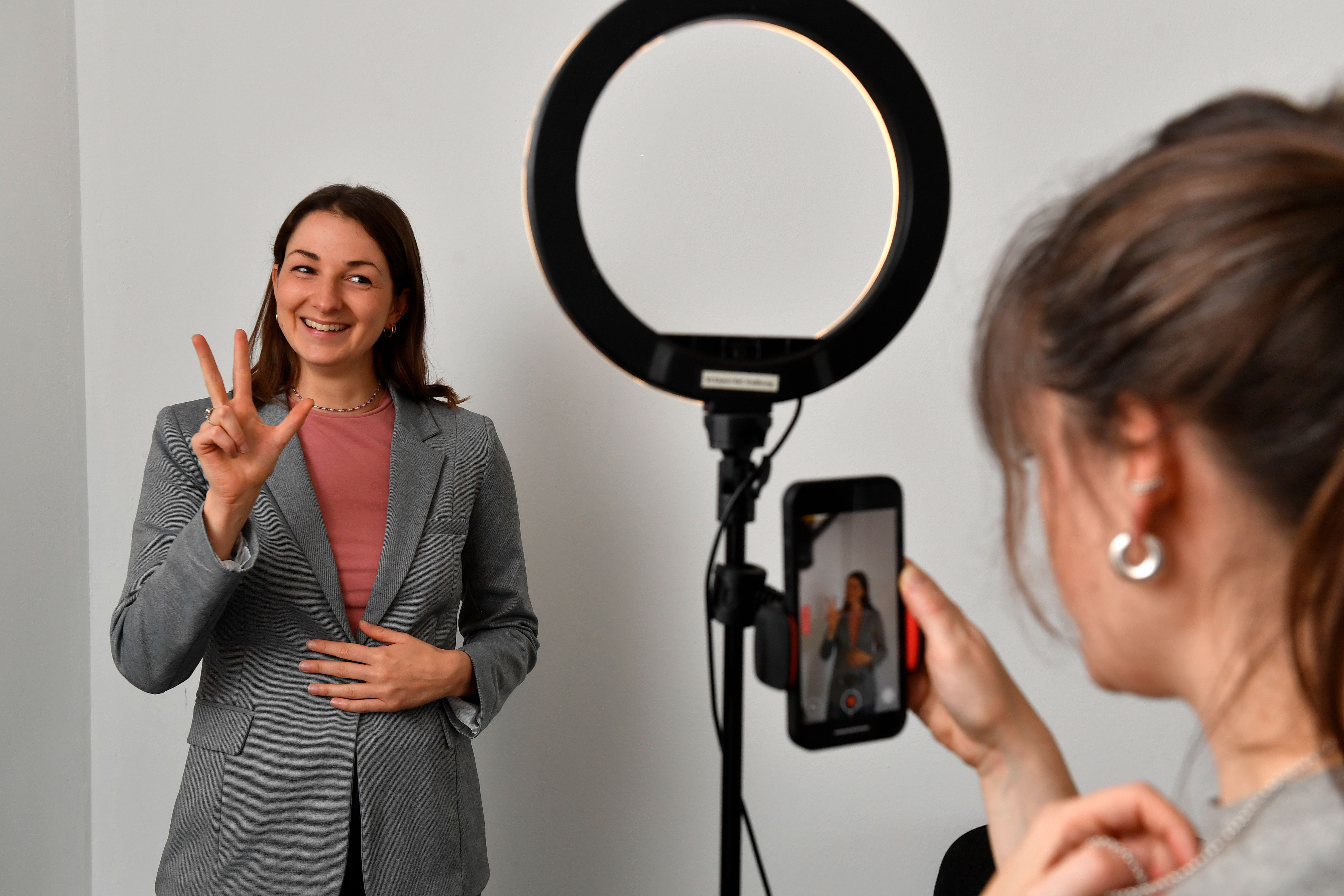 Ein Dreh für Social Media. Die Protagonistin hält drei Finger nach oben. Eine weitere Frau bedient das Handy und blickt auf das Display.