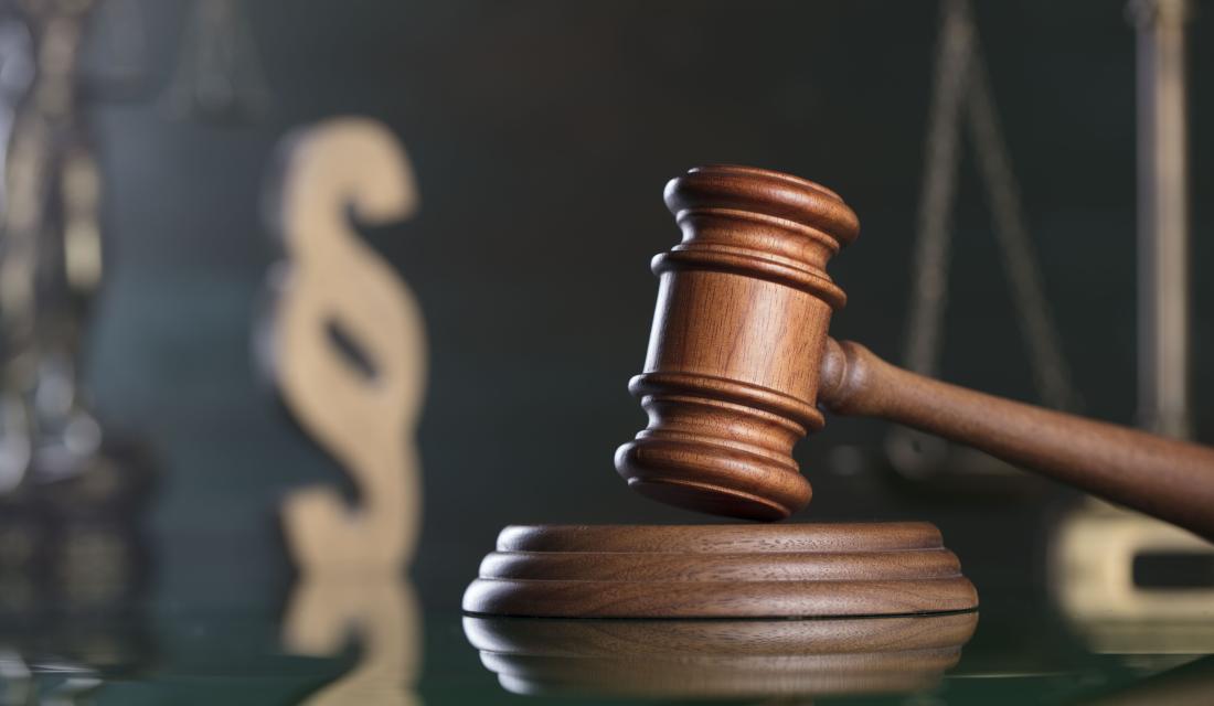 Ein Hammer im Gerichtssaal, dahinter ein Paragraph als Holzfigur