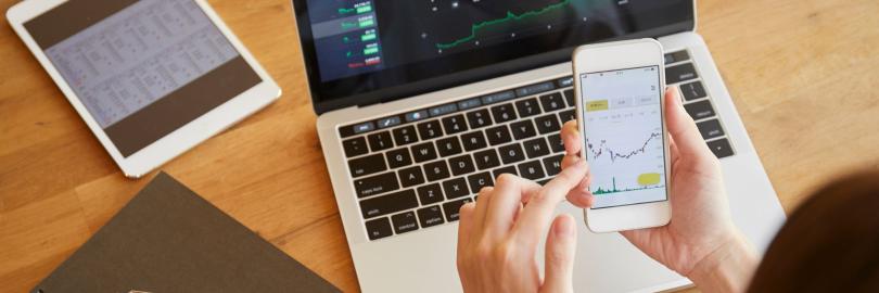 Jemand schaut sich Aktienkurse auf dem Laptop und dem Handy an