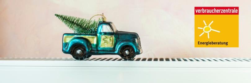 Ein Christbaumanhänger als Pick up mit einem kleinen Weihnachtsbaum auf der Ladefläche steht auf einer Heizung.