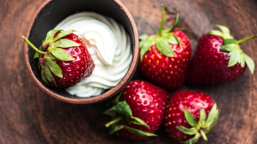Eine Schüssel mit Sahne steht auf einem Tisch. In der Schüssel liegt eine, neben der Schüssel liegen vier Erdbeeren.