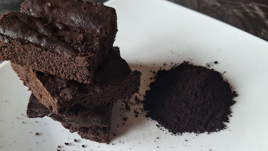 Ein Schokokuchen liegt auf einem Teller, daneben ein Häufchen mit schwarzem Kakaopulver