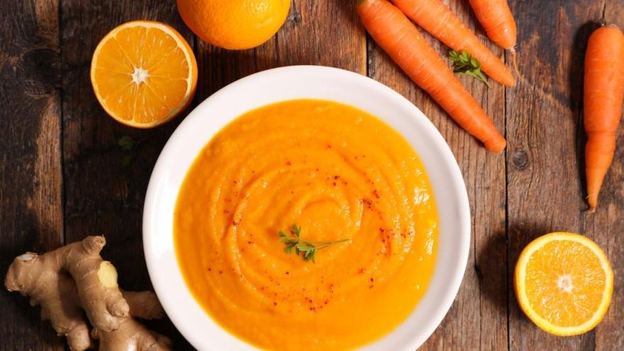 Ein Teller Möhrensuppe, daneben liegen Ingwer, Orangen und Möhren