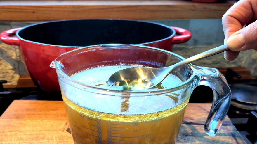 Mit einem Löffel wird das Fett der kalten Soße abgeschöpft