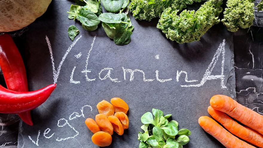Verschiedene Vitamin A-haltige Gemüse wie Spinat und Möhren liegen auf einer schwarzen Schiefertafel auf der "Vitamin A" und "vegan" steht.