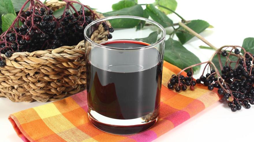 Ein Glas mit Holundersaft steht auf einem bunt kariertem Geschirrtuch, daneben Zweige mit Holunderbeeren.