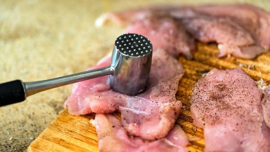 Rohe Schnitzel, mit Fleischzartmacher gewürzt, liegen auf einem Brett. Ein Fleischklopfer ruht auf einem Schnitzel.