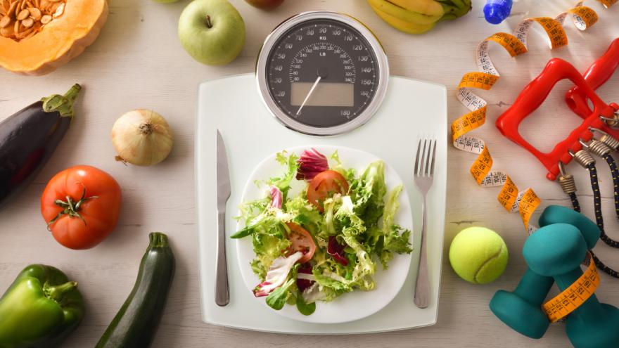 Auf einer Körperwaage steht ein Teller mit Salat, links und rechts daneben liegen Messer und Gabel.