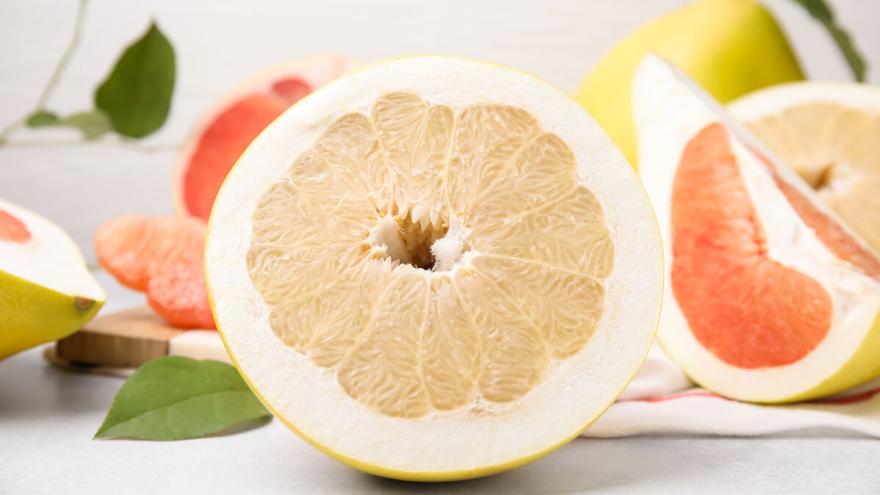 Halbierte Pomelos liegen auf einem weißen Tisch.