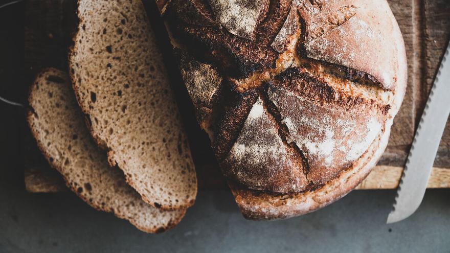 Ein Laib Bauernbrot liegt auf einem Holzbrett, daneben ein Messer. Zwei Scheiben sind vom Laib abgeschnitten.