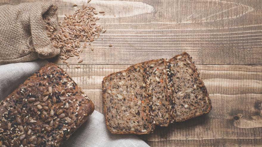 Zwei Scheiben Körnerbrot liegen auf einem Holzbrett, darüber ein Sack mit Körnern.