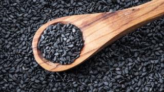 Um und auf einem Holzlöffel liegen schwarze Sesamkörner.