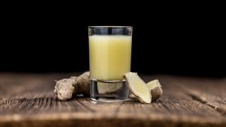 Ein Glas mit einem Ingwershot steht auf dem Tisch, daneben liegen Ingwerwurzeln.