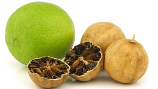 Eine aufgeschnittene schwarze Zitrone liegt neben zwei ganzen schwarzen Zitronen und einer Limette.