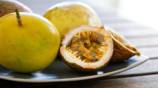 Mehrere Passionsfrüchte, eine davon halbiert, liegen auf einem Teller.