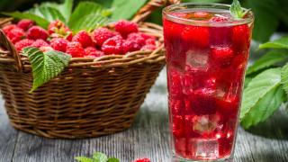 Neben einem Korb mit Himbeeren steht ein Glas mit Himbeer-Shrub