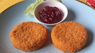 Zwei Scheiben gebackener Camenbert und eine kleine Schüssel mit Preiselbeeren auf einem Teller. 