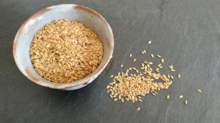 Eine helle Schüssel mit Leinsamen steht auf einem Tisch, neben der Schüssel liegen ebenfalls einige Leinsamenkörner