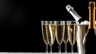 Fünf gefüllte Sektgläser stehen neben einer Sektflasche und einem Sektkübel, in dem sich ebenfalls eine Sektflasche befindet