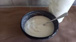 Eine schwarze Müslischüssel mit Naturjoghurt und einem Löffel darin steht auf einer Küchenarbeitsplatte