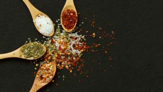 Vier Holzlöffel, gefüllt mit verschiedenen Gewürzen liegen auf einem schwarzen Tisch