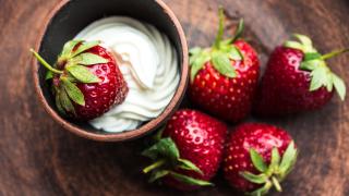 Eine Schüssel mit Sahne steht auf einem Tisch. In der Schüssel liegt eine, neben der Schüssel liegen vier Erdbeeren.