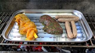 In einer Aluschalen liegen ein Spieß, ein Stück Grillfleisch und Grillwürstchen.