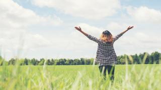 Eine junge Frau steht mit offenen Armen auf einem Feld.