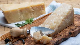 Zwei Stück Parmesan liegen auf zwei Brettern. Das vordere Stück ist mit einem Käsemesser angeschnitten.