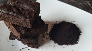 Ein Schokokuchen liegt auf einem Teller, daneben ein Häufchen mit schwarzem Kakaopulver