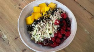 Ein Schüssel mit Haferbrei steht auf einem Tisch. Garniert ist der Brei mit Mango, Beeren und Zucchini.