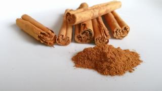 Sechs Cassia-Zimtstangen liegen auf einer weißen Fläche; davor ein Häufchen gemahlener Zimt