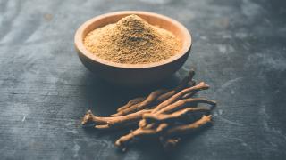 In einer Schale befindet sich Ashwagandha-Pulver, daneben liegt die Wurzel.