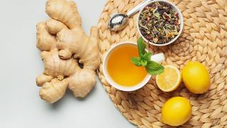 Neben einer Tasse Tee liegen eine Ingwerwurzel und Zitronen