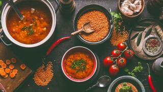 In verschiedenen Töpfen sieht man gekochte und rohe rote Linsen, daneben Zutaten wie Karotten, Tomaten oder Knoblauch