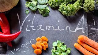 Verschiedene Vitamin A-haltige Gemüse wie Spinat und Möhren liegen auf einer schwarzen Schiefertafel auf der "Vitamin A" und "vegan" steht.