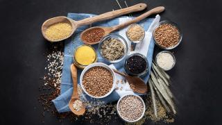 Verschiedene Gertreidekörner stehen in kleinen Schüsseln auf einem Tisch.