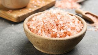 Eine Holzschüssel mit rotem Hawaii-Salz steht auf einer schwarzen Arbeitsfläche.