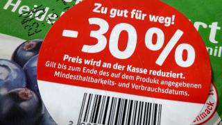 Runder roter Aufkleber auf einem Joghurtbecherdeckel, Aufkleber-Aufschrift: "Zu gut für weg! -30 % Preis wird an der Kasse reduziert. Gilt bis zum Ende des auf dem Produkt angegebenen Mindesthaltbarkeits- und Verbrauchsdatums."