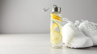 Eine Trinkflasche, die mit Wasser und Zitronenscheiben gefüllt ist, steht neben einem Paar weißer Turnschuhe.