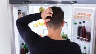 Ein Mann guckt in einen geöffneten Kühlschrank und kratzt sich dabei am Kopf.