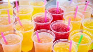 Mehrere Becher mit gelbem, orangefarbenem und rotem Slush Ice stehen nebeneinander.