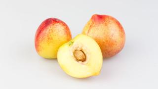 Zwei ganze und ein halber Pfirsich mit Kern auf einer weißen Fläche.