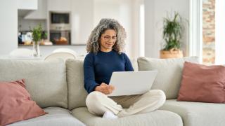 Eine Frau sitzt im Schneidersitz auf einem Sofa mit dem Laptop auf dem Schoß