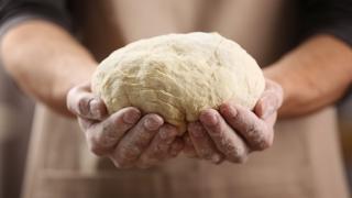 Zwei Hände halten einen rohen Hefeteig.