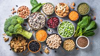 Bohnen, Linsen, Nüsse, Brokkoli, Spinat, Samen und weitere vegane Proteinquellen liegen auf einem Tisch. 