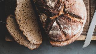 Ein Laib Bauernbrot liegt auf einem Holzbrett, daneben ein Messer. Zwei Scheiben sind vom Laib abgeschnitten.